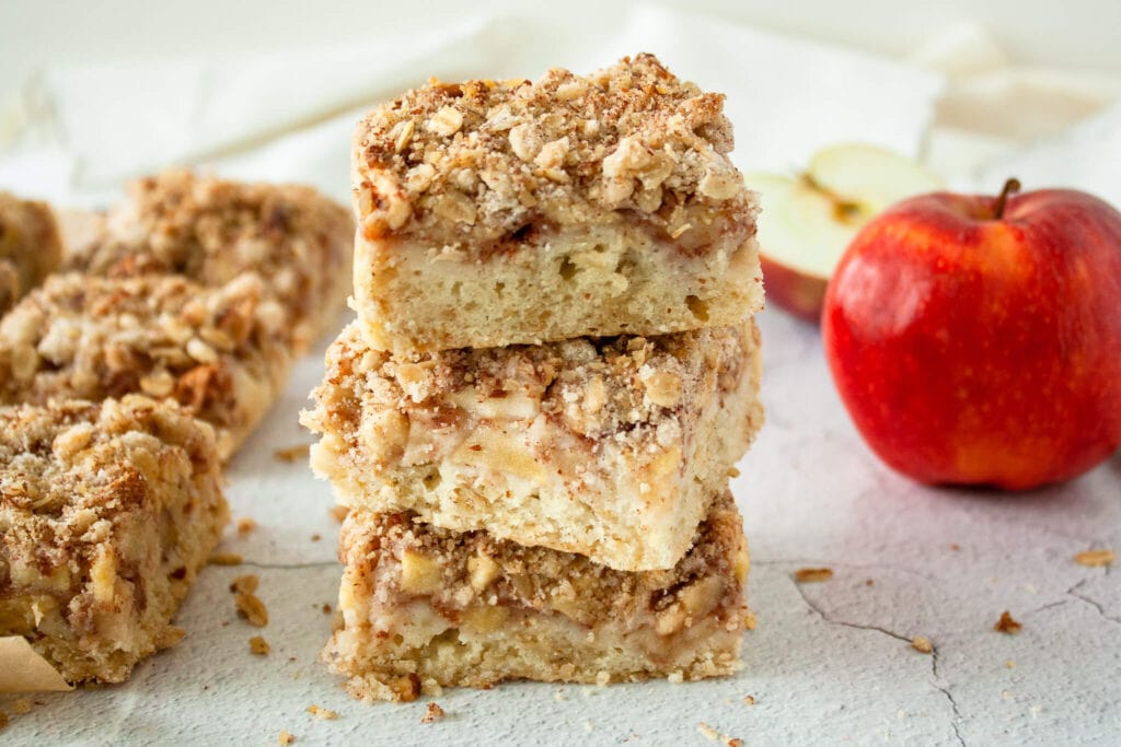 Decorative photo of stacked apple crisp bars with a red apple in the background